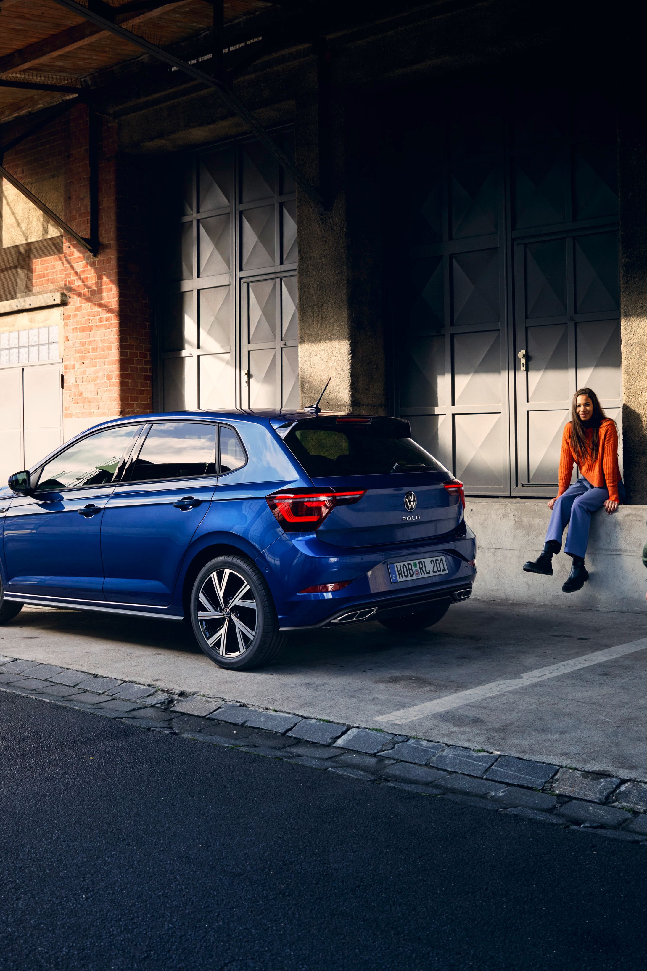 Ein blauer VW Polo steht vor einer Rampe, ein Mann geht am Heck mit den optionalen LED-Rückleuchten vorbei. 