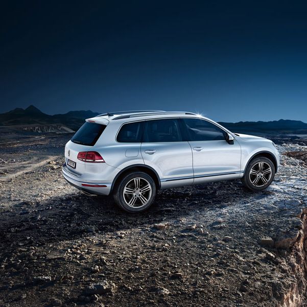 Бял Volkswagen Touareg, спрян на скалист ръб с гледка към дълбок каньон под звездно небе.