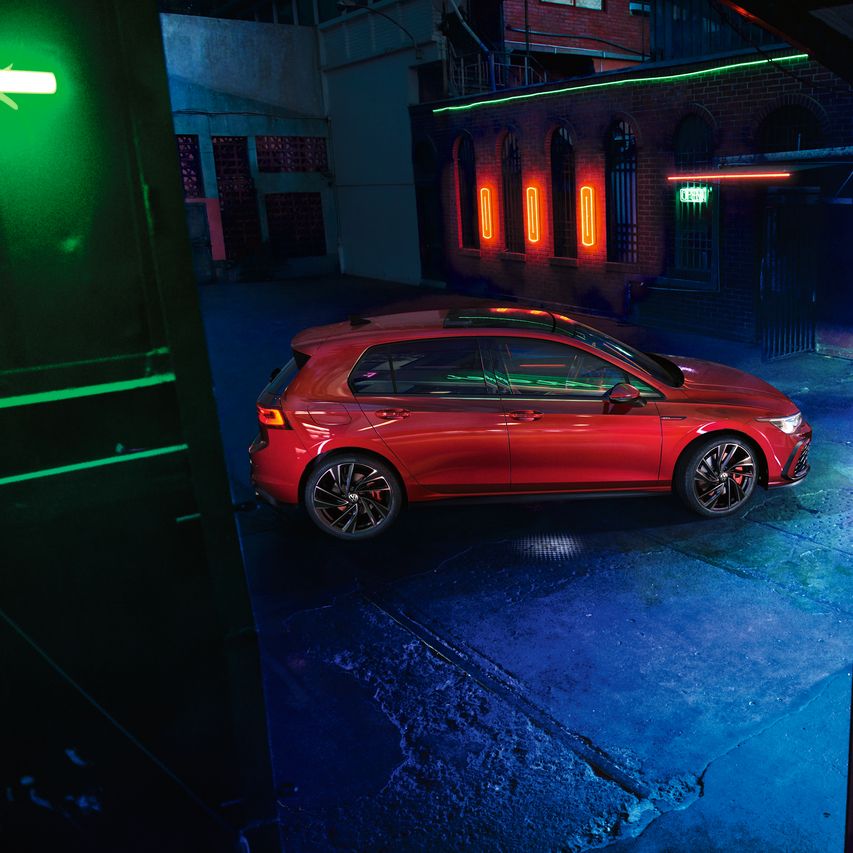 Червен Volkswagen Golf GTI, заснет отстрани в индустриална обстановка с ефектно неоново осветление