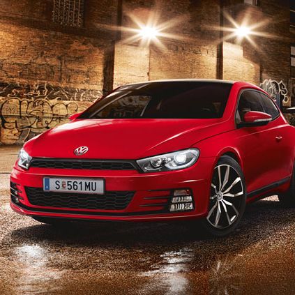 Червено спортно купе Volkswagen, паркирано на мокра улица с графити и нощно осветление.