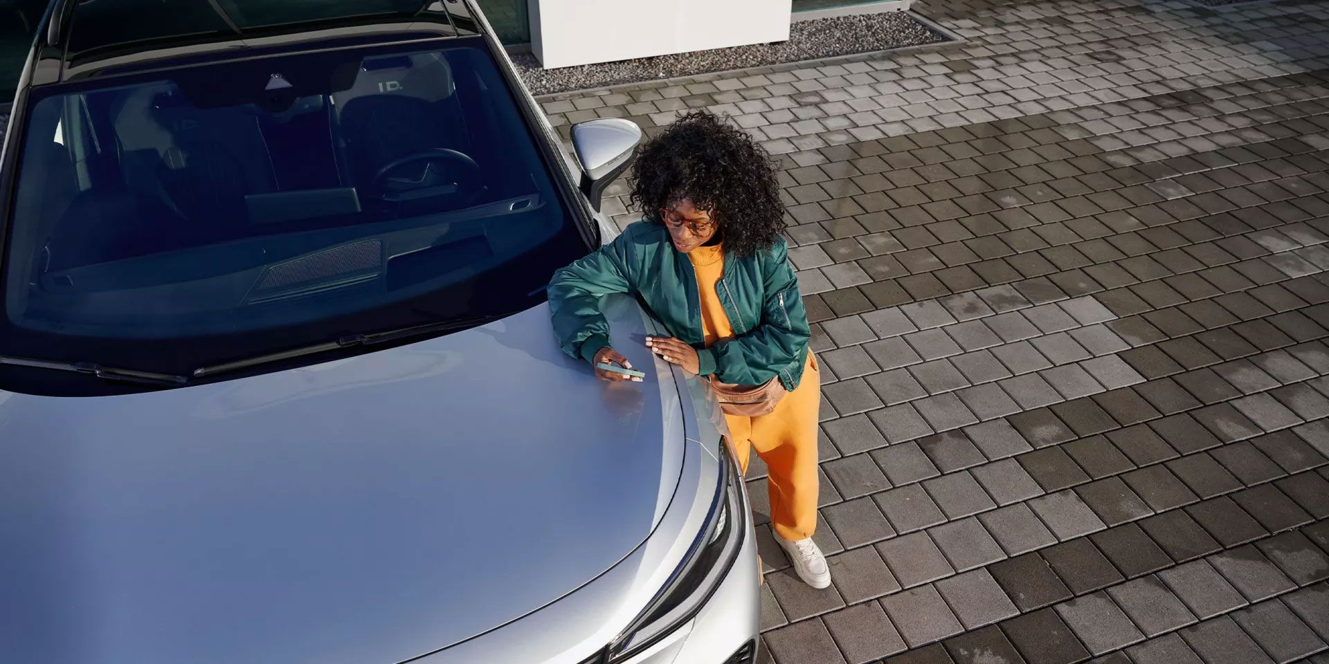 Поглед отгоре на VW ID., жена се е облегнала на предния капак