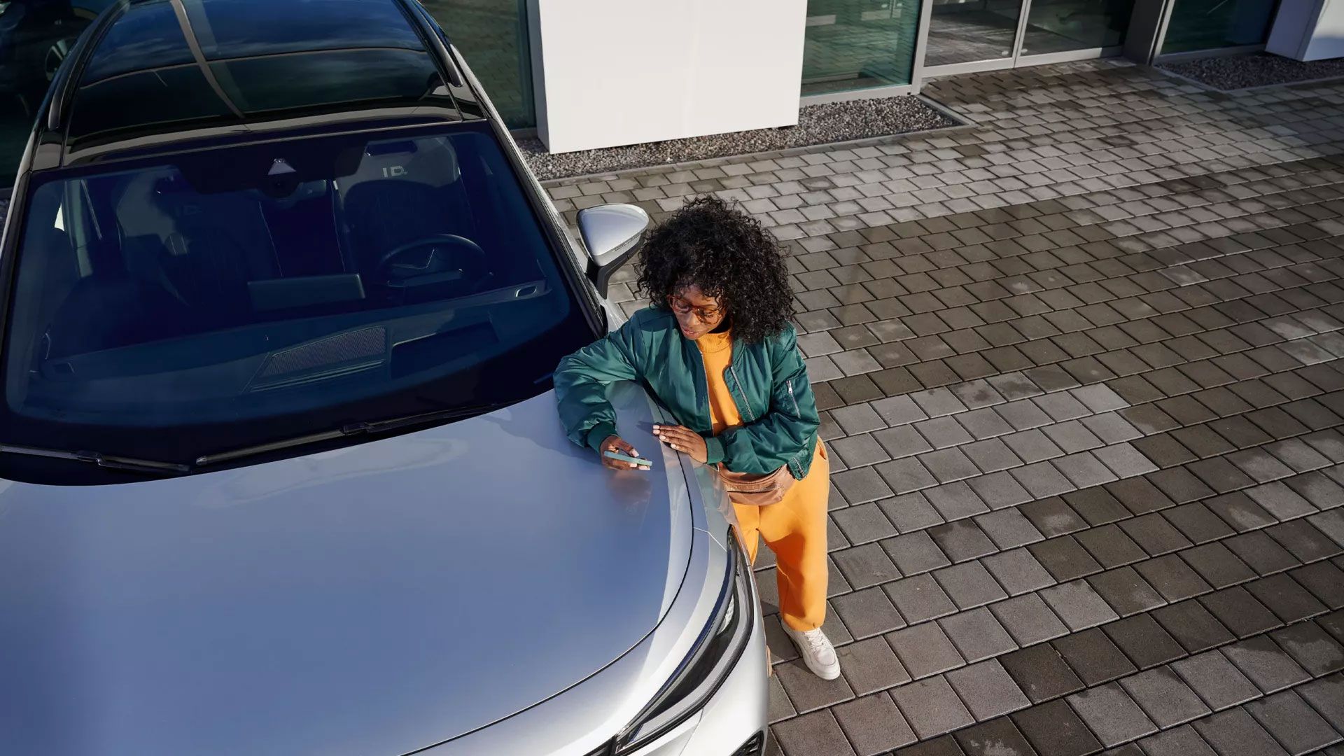 Поглед отгоре на VW ID., жена се е облегнала на предния капак