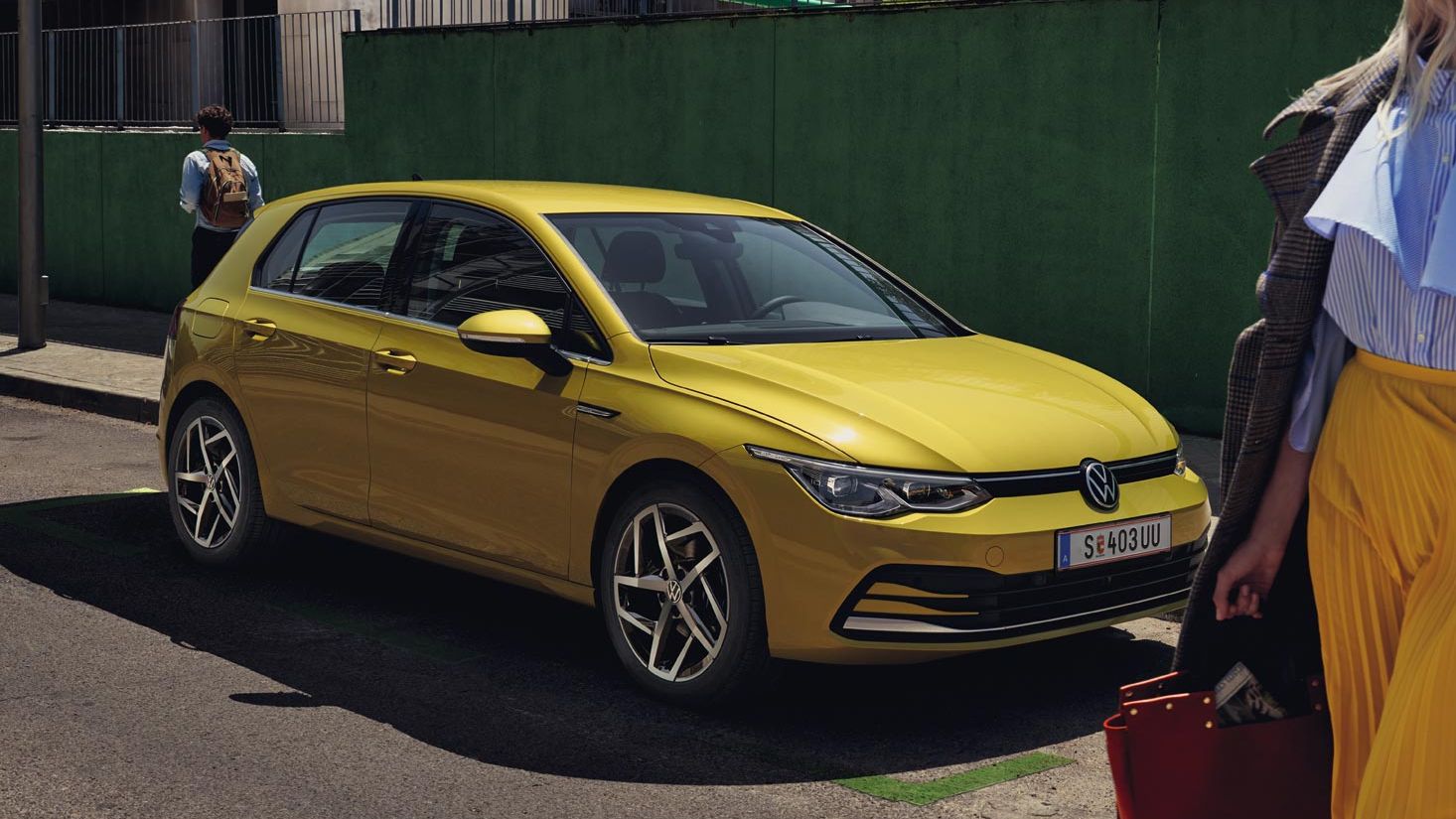Жълт Volkswagen Golf паркиран на градска улица с модерно облечена жена на преден план