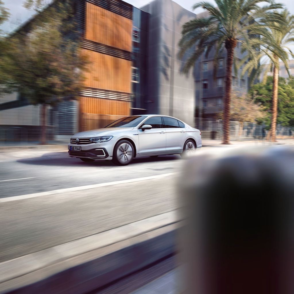 Сребрист Volkswagen Passat в движение по градска улица с палми