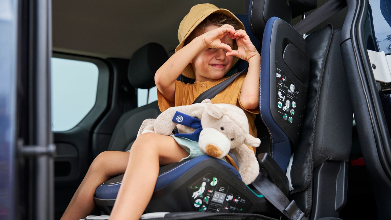 Дете в детско столче на задната седалка на Volkswagen, държащо плюшена играчка.