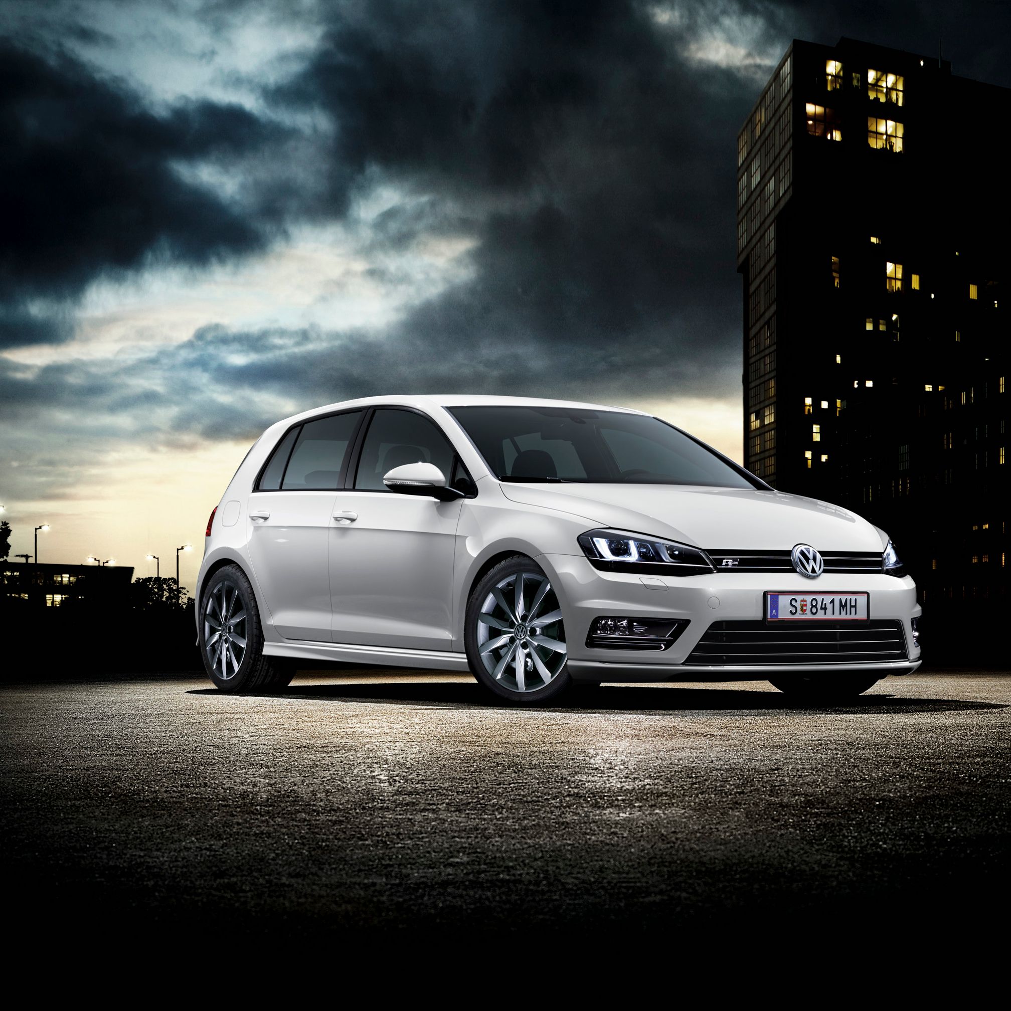 Бял Volkswagen Golf паркиран в градска среда на фона на нощно небе и осветени сгради