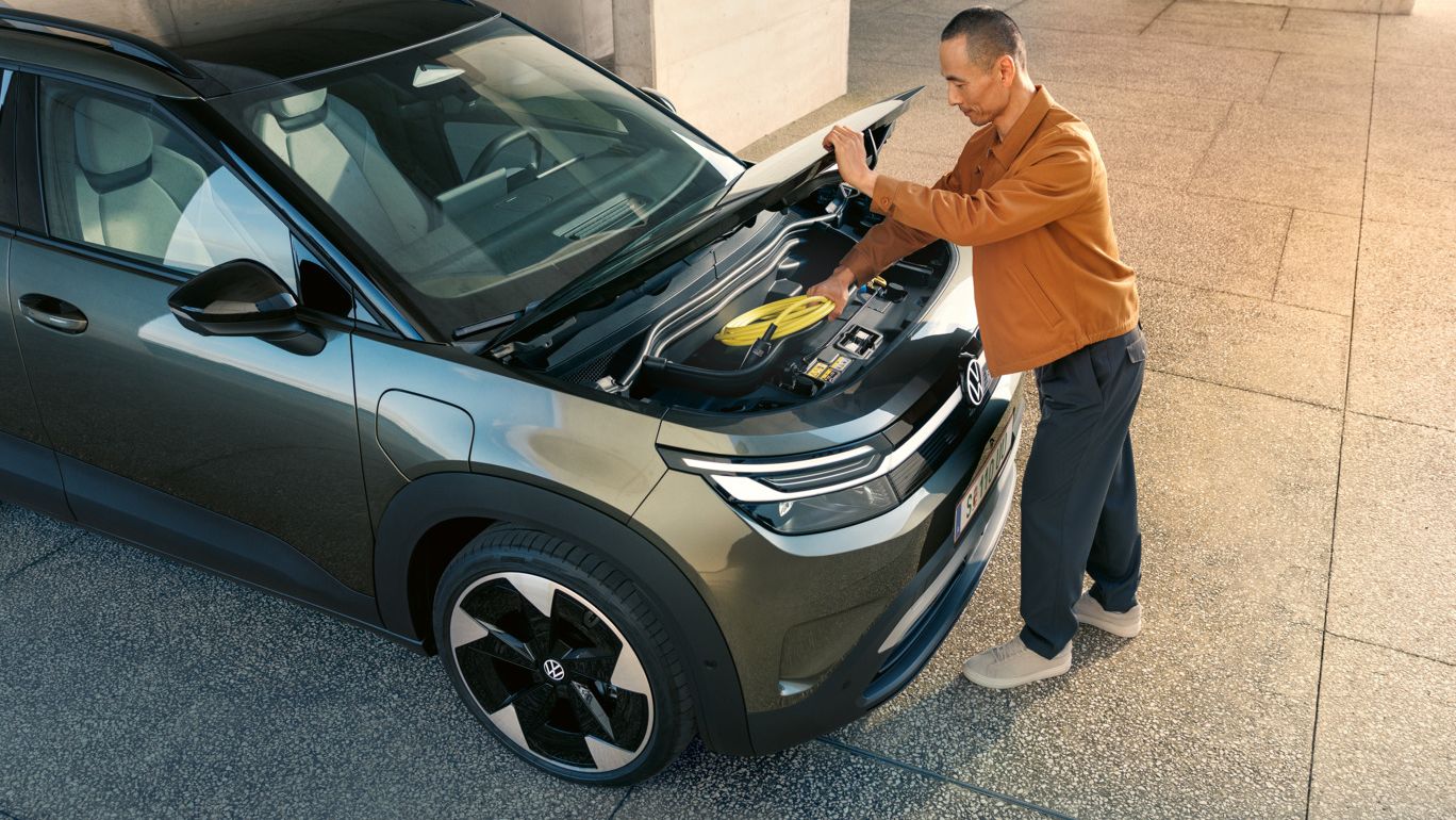 Мъж отваря зелен VW ID. Cross, за да извади кабела за зареждане