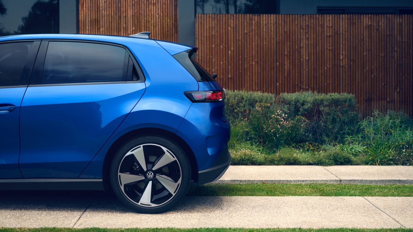 Страничен изглед назад на син VW ID. Поло стил, стоящ пред жилищна сграда с зелена алея.