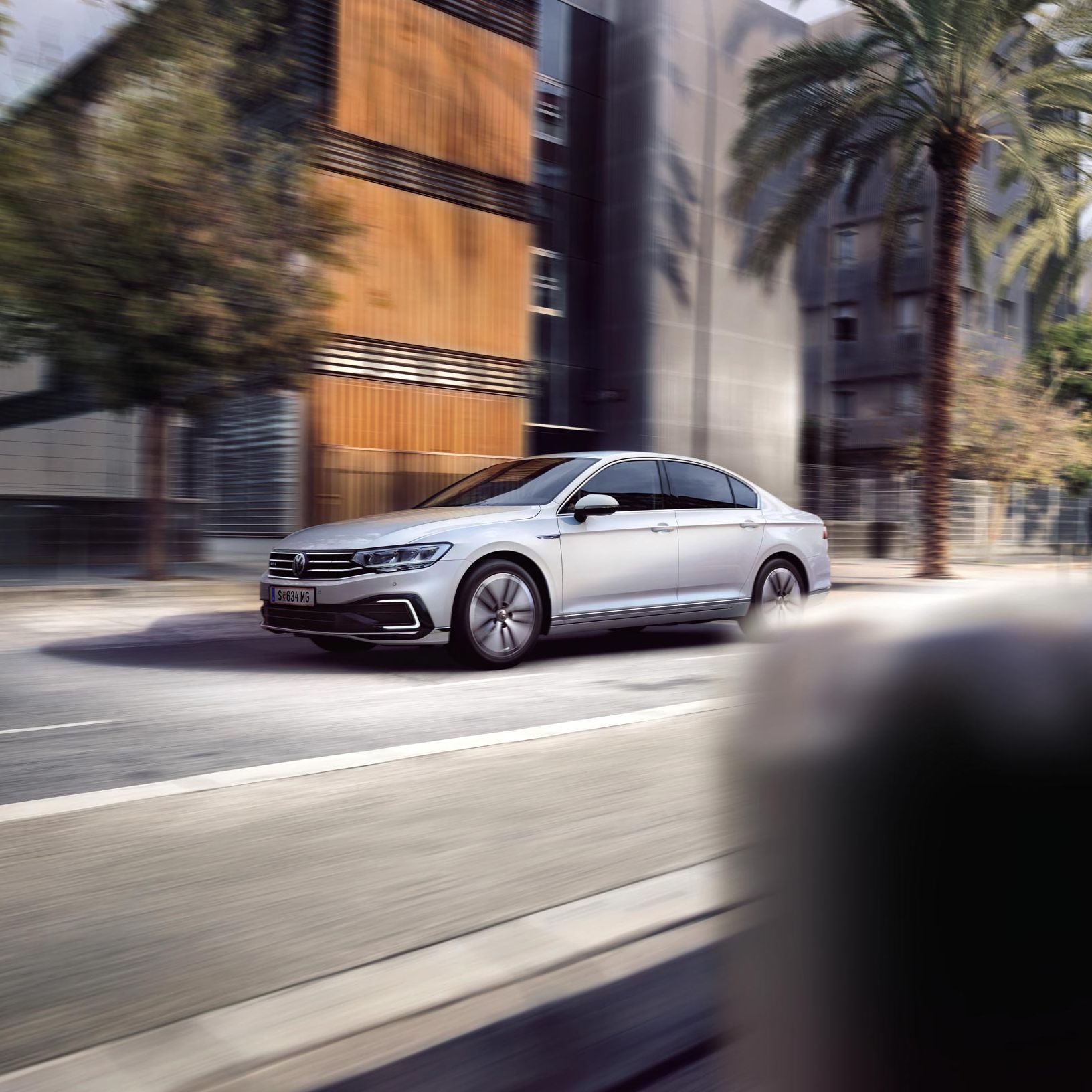 Сребрист Volkswagen Passat в движение по градска улица с палми