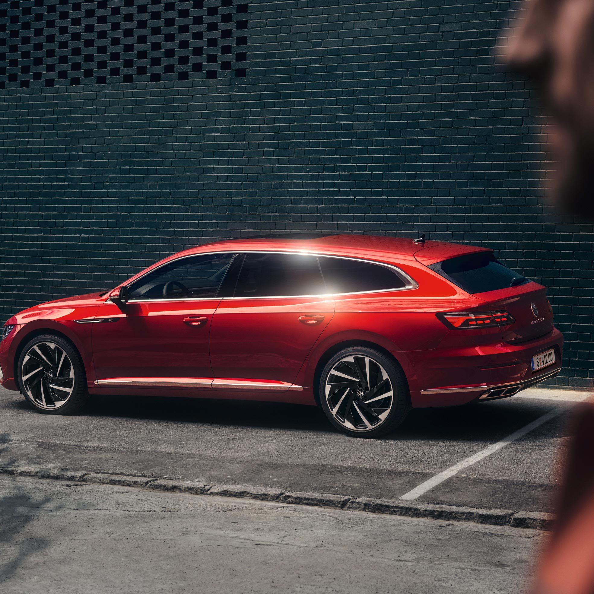 Стилен червен Volkswagen Arteon Shooting Brake паркиран до модерна тъмна стена