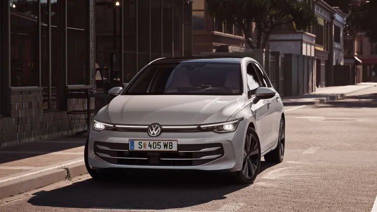 Weißer VW Golf fährt auf einer Straße auf eine Kreuzung zu.