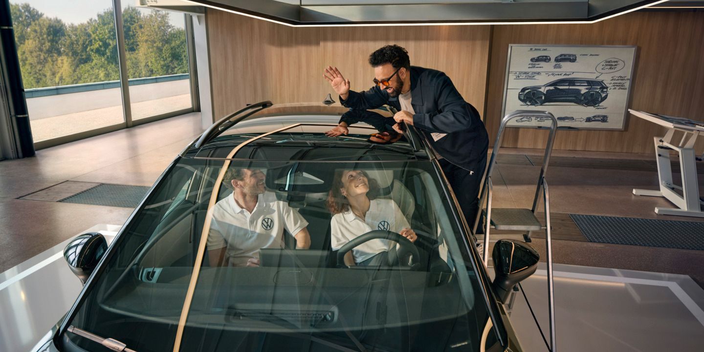 Мъж стои на стълба до VW ID. Cross и маха през панорамния покрив на хората, които седят вътре в автомобила.