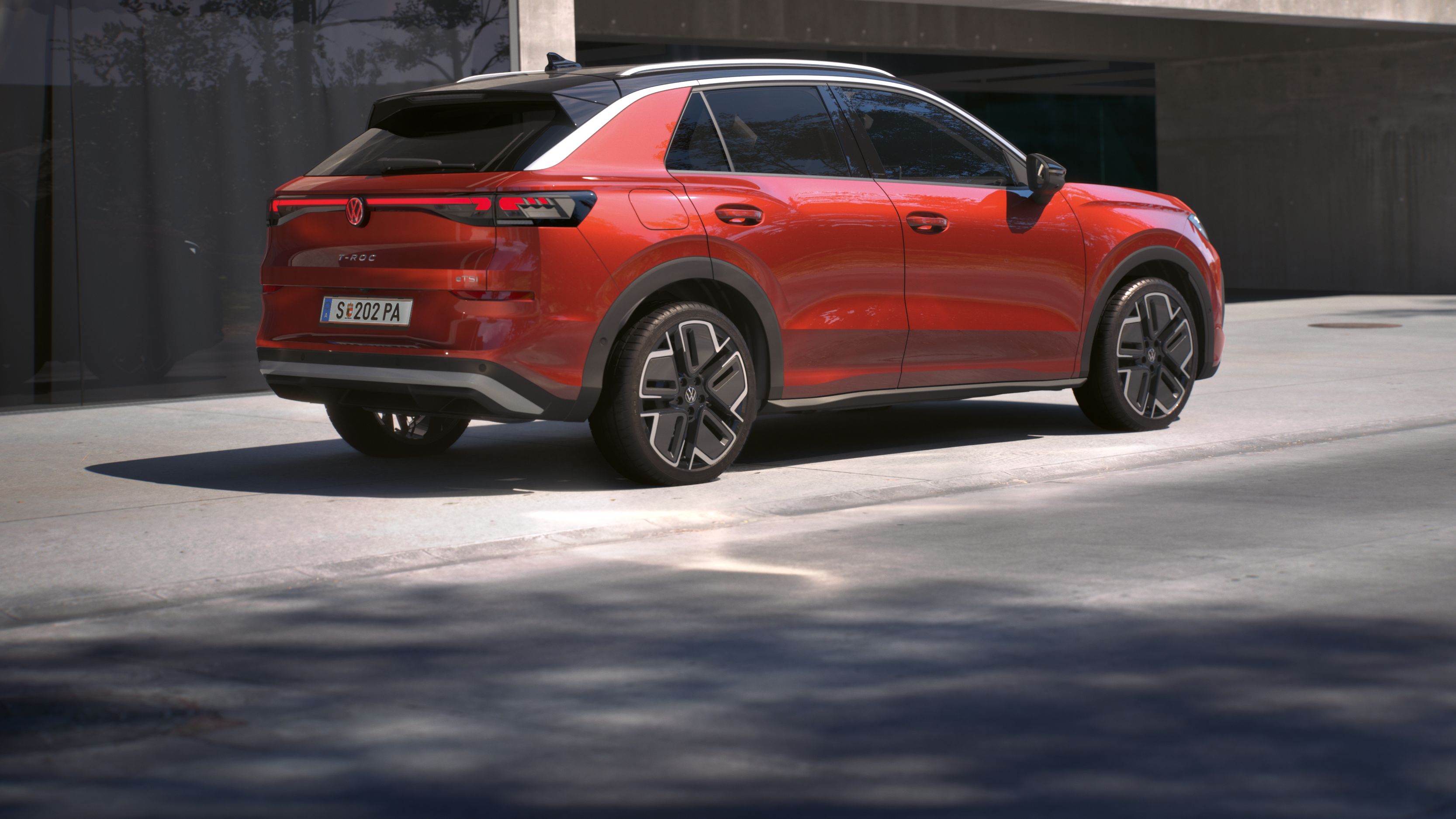 Червен Volkswagen T-Roc паркиран пред модерна сграда, изглед отзад.