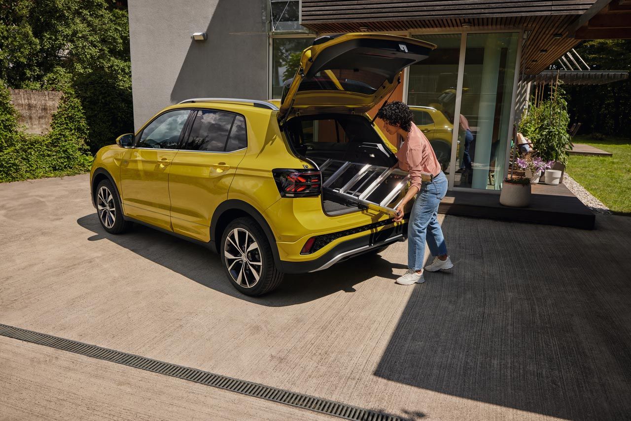Eine junge Frau schiebt eine Leiter in den Kofferraum eines gelben VW T-Cross.