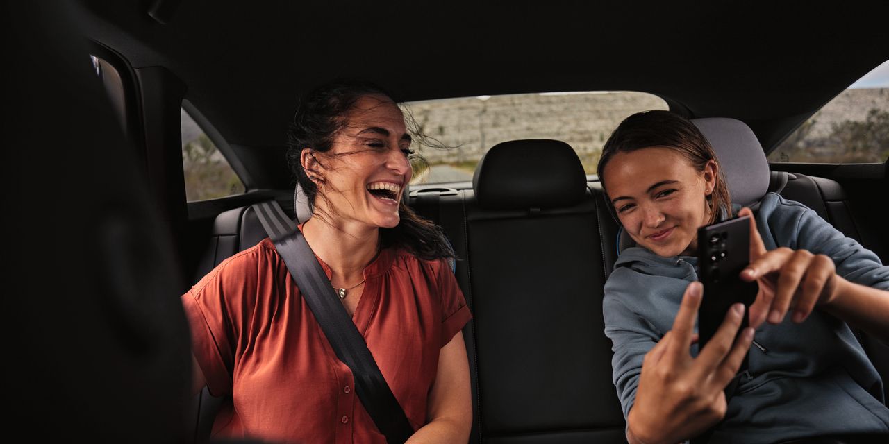  Двама души седят на задната седалка на Volkswagen и гледат в мобилен телефон с усмивка на лицето