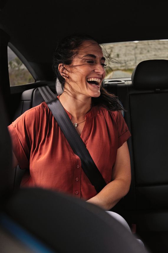 Двама души седят на задната седалка на Volkswagen и гледат в мобилен телефон с усмивка на лицето