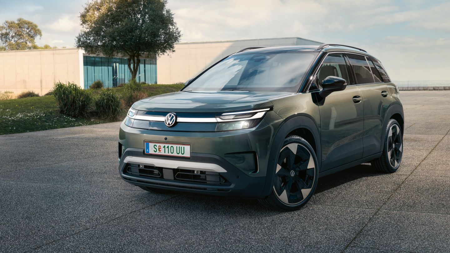 Зелен VW ID. Cross стои пред модерна стъклена сграда върху бетонна повърхност.