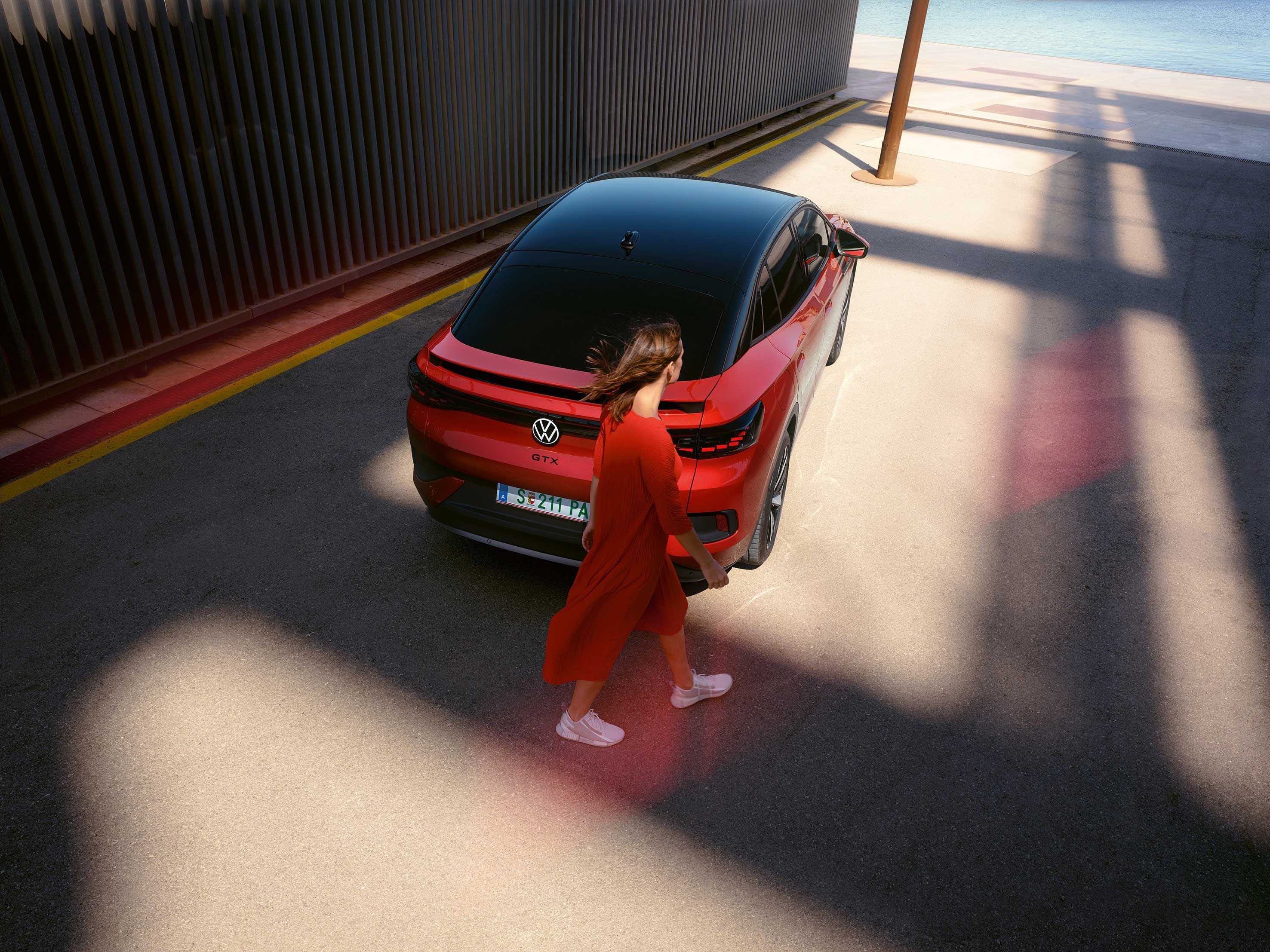 Frau geht am Heck eines roten VW ID.5 GTX vorbei