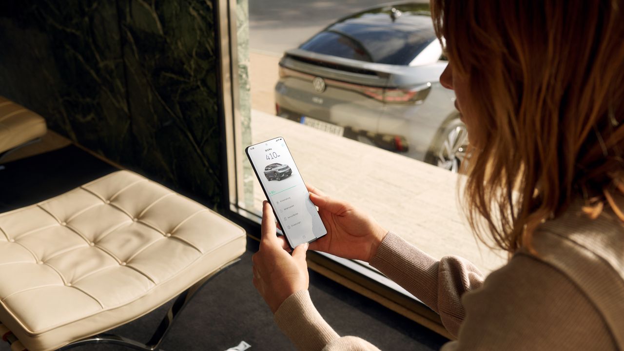 Изглед отзад на сив VW ID.5, на преден план жена ползва смартфон