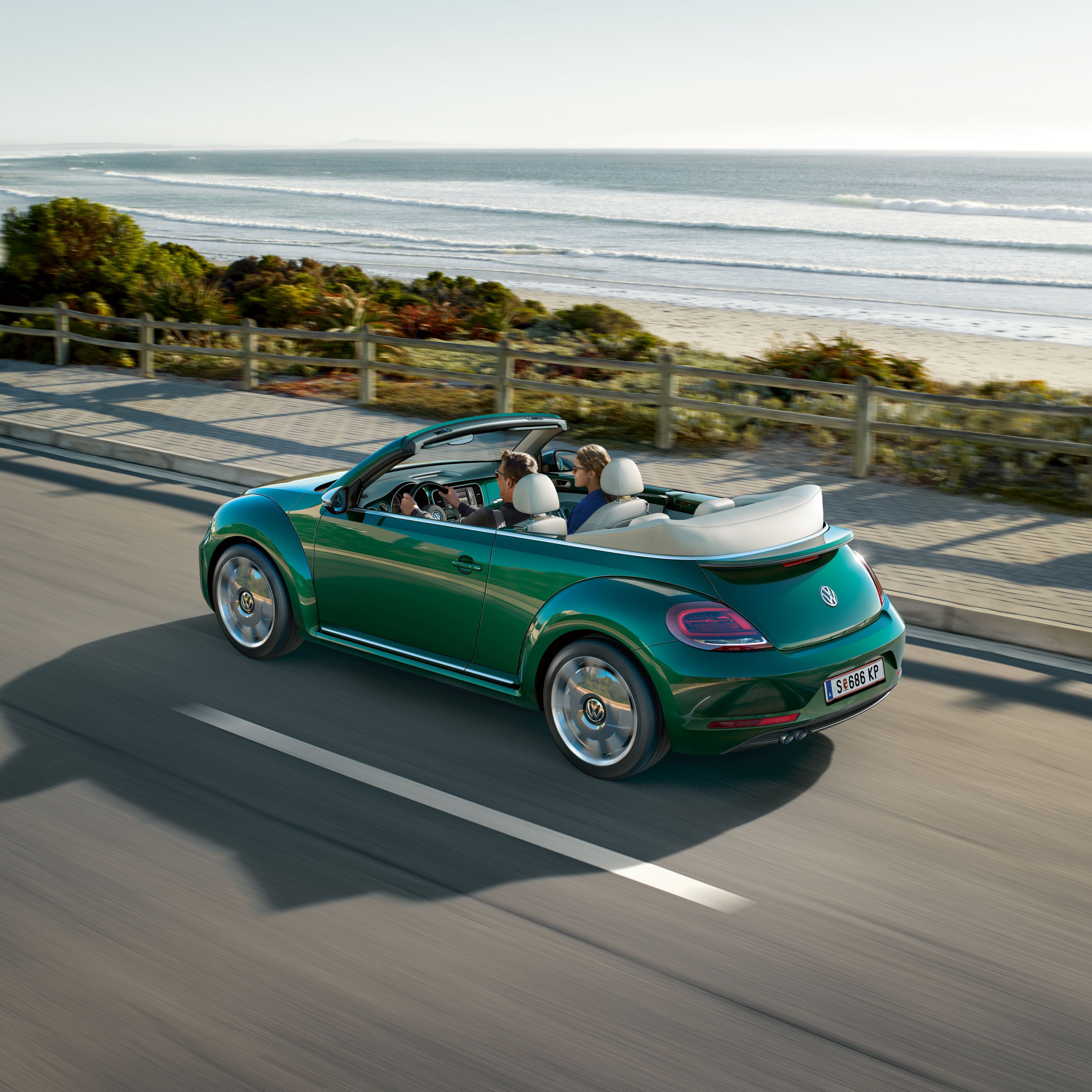 Зелен Volkswagen Beetle кабриолет в движение по крайбрежен път с отворен покрив.