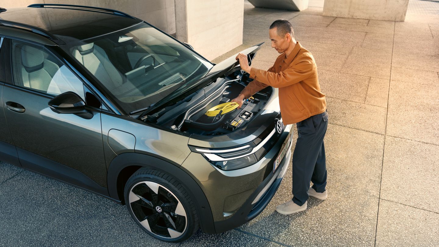 Мъж отваря зелен VW ID. Cross, за да извади кабела за зареждане