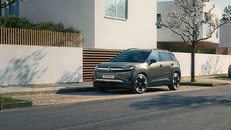 Зелен VW ID. Cross е паркиран на паркинг в жилищен район с цъфтящи дървета.