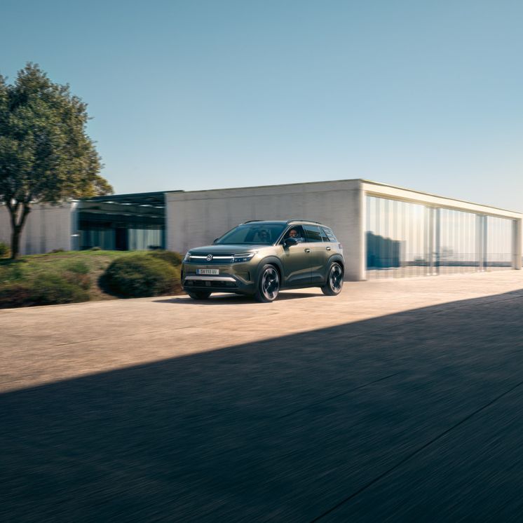 Зелен VW ID. Cross кара по алея на модерна жилищна сграда.
