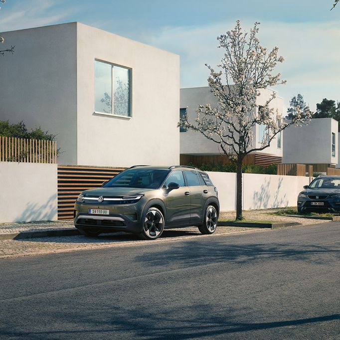 Зелен VW ID. Cross е паркиран на паркинг в жилищен район с цъфтящи дървета.