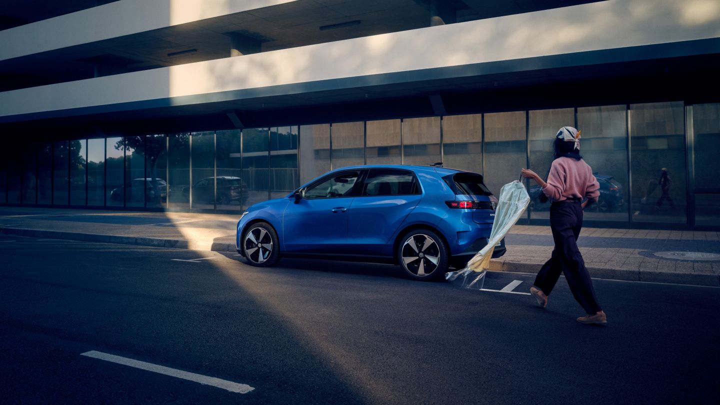 Син VW ID. Polo Style е паркиран край пътя, жена се приближава към автомобила.