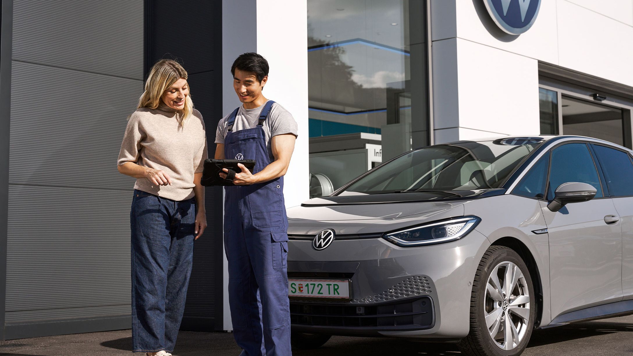 Сервизен консултант на Volkswagen показва информация на клиент до електрически автомобил Volkswagen ID.3 пред дилърски център.