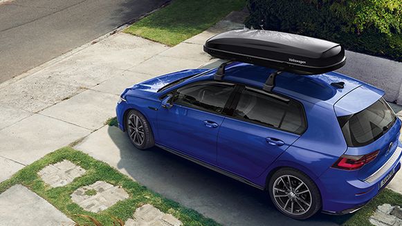 Син Volkswagen Golf с багажник на покрива, паркиран пред къща.