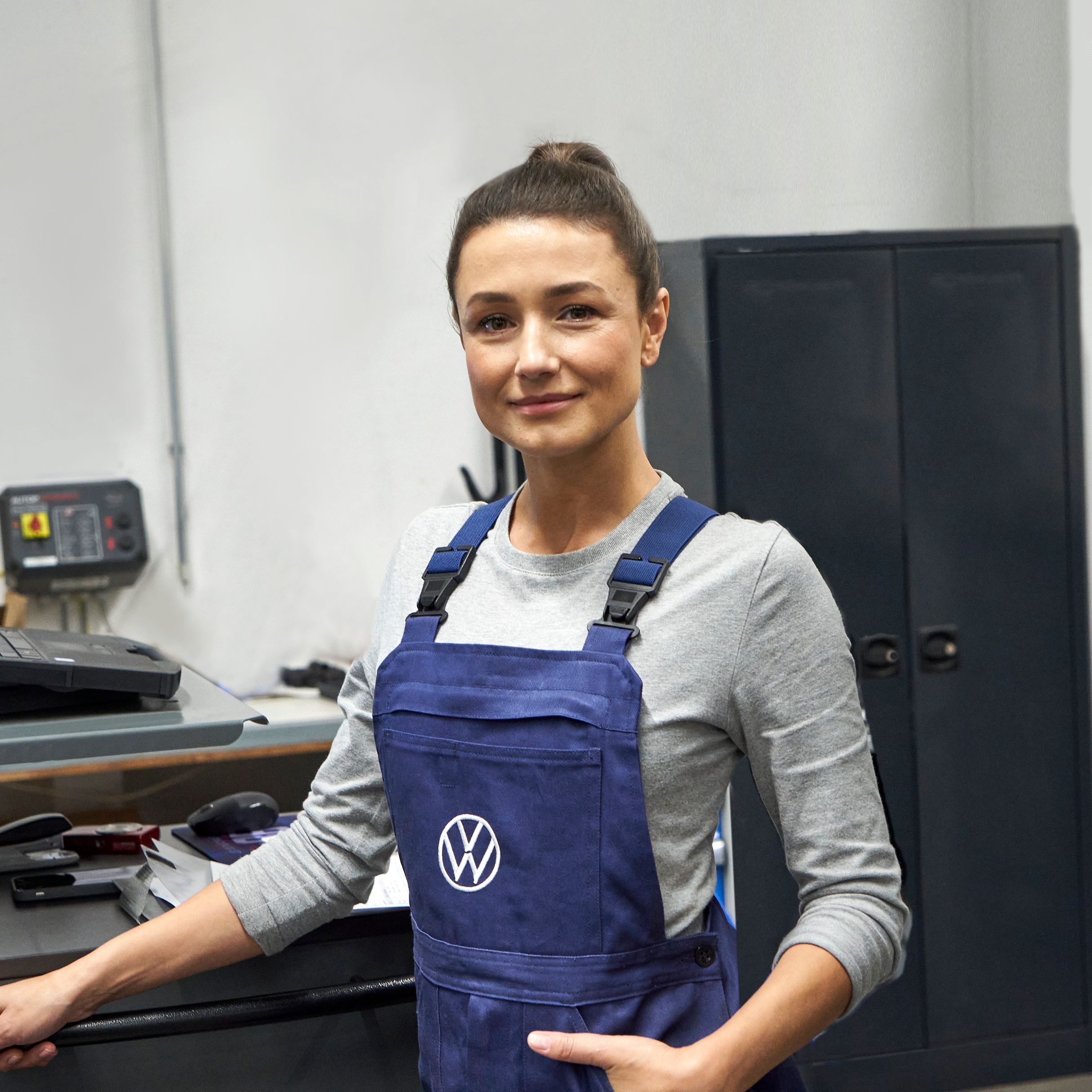 Жена сервизен механик облечена в син гащирезон с лого на Volkswagen до бюро с техническо оборудване