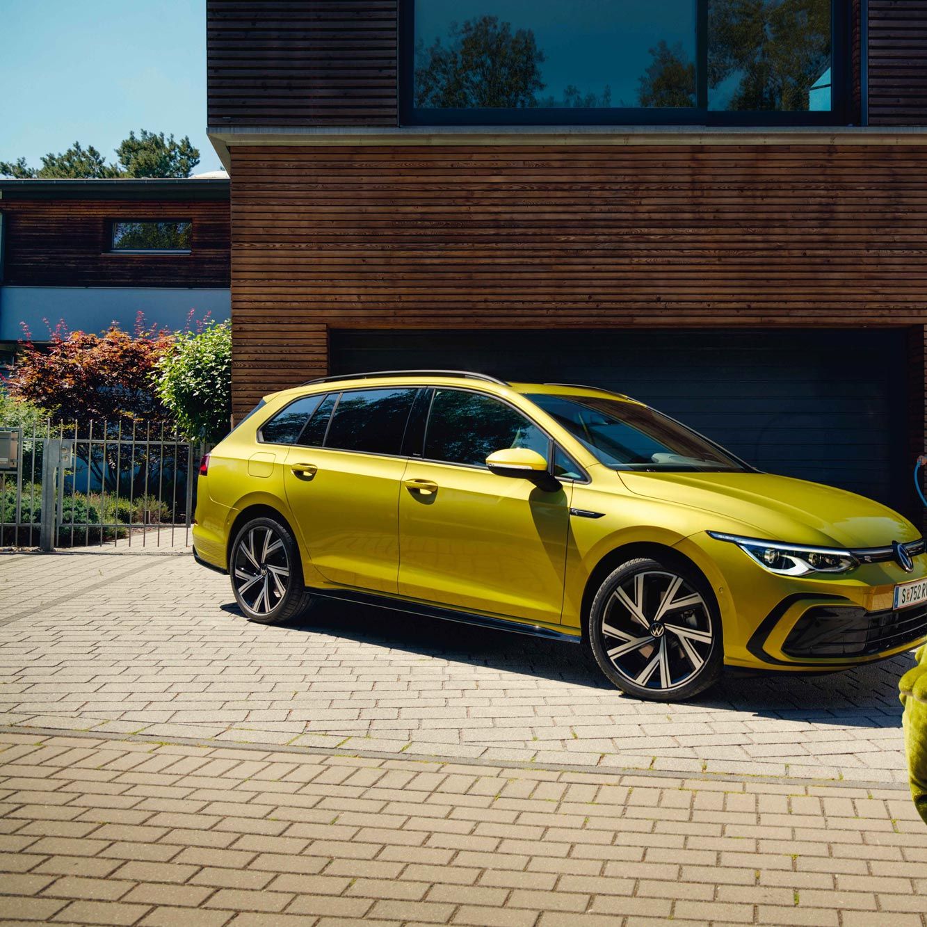 Момче с голяма плюшена играчка пред жълт Volkswagen Golf Variant, паркиран пред модерен дом