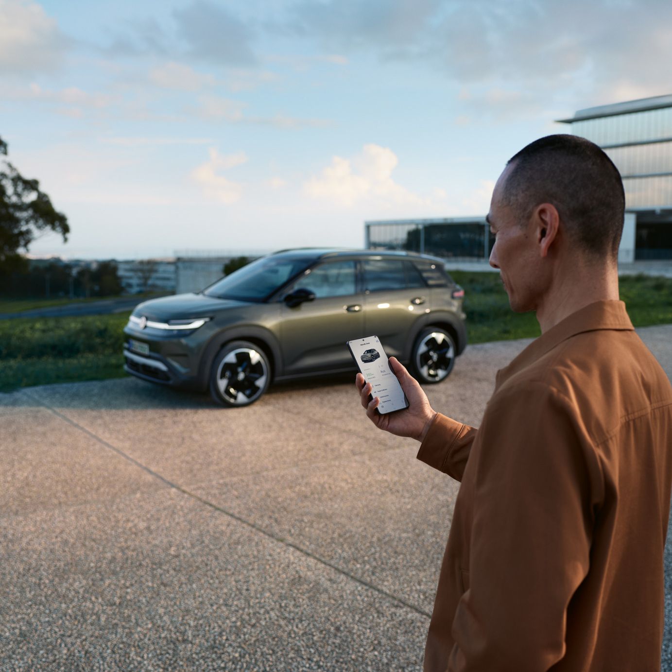 Зелен VW ID.Cross е паркиран пред жилищна сграда, до него стои мъж, който гледа смартфона си.