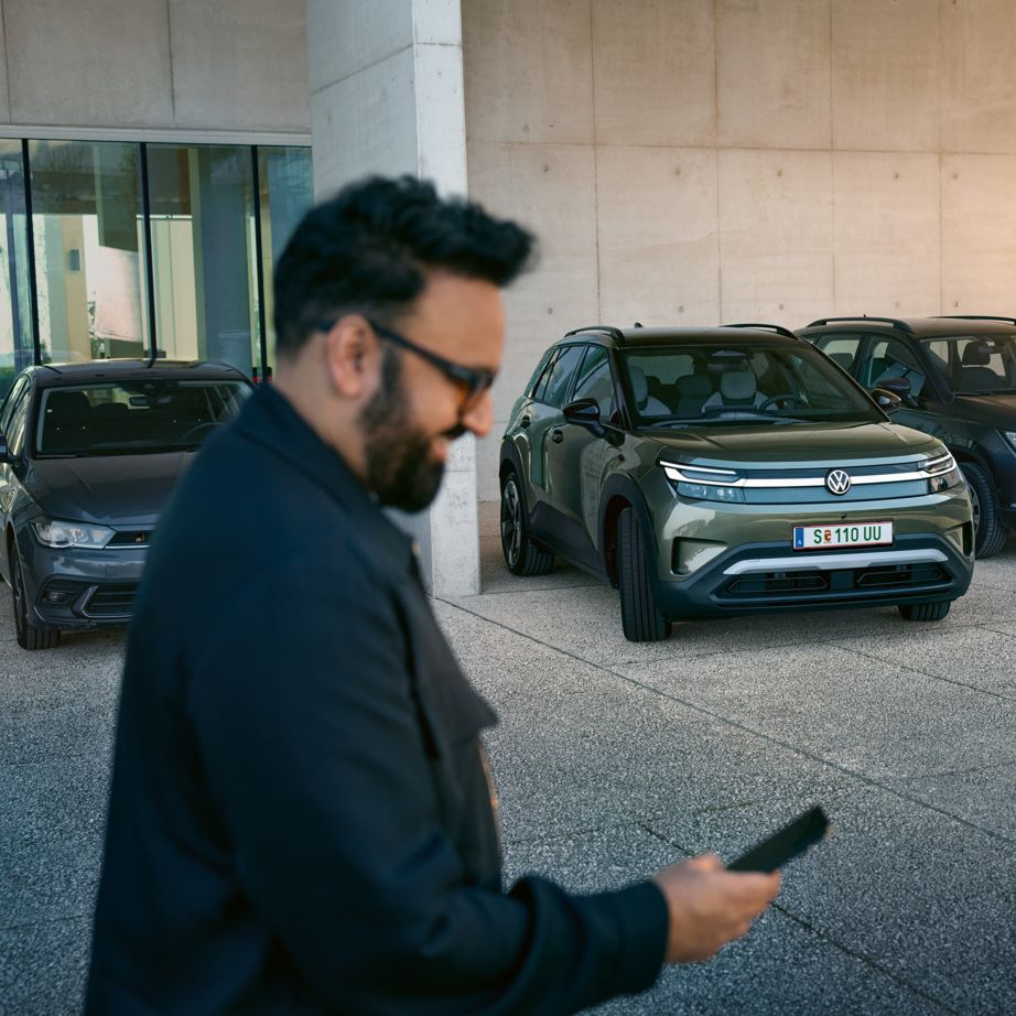 Мъж гледа смартфона си, на заден план има VW ID. Cross автоматично влиза в паркомясто.