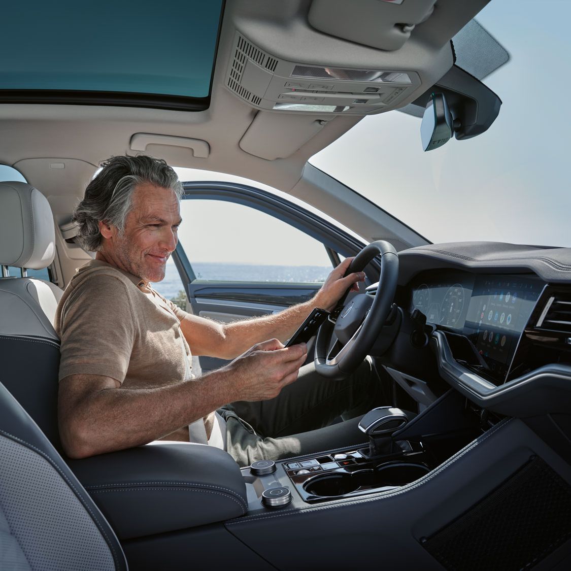 Мъж в паркиран VW Touareg Elegance свързва своя смартфон с VW Touareg Elegance чрез Wireless App Connect.