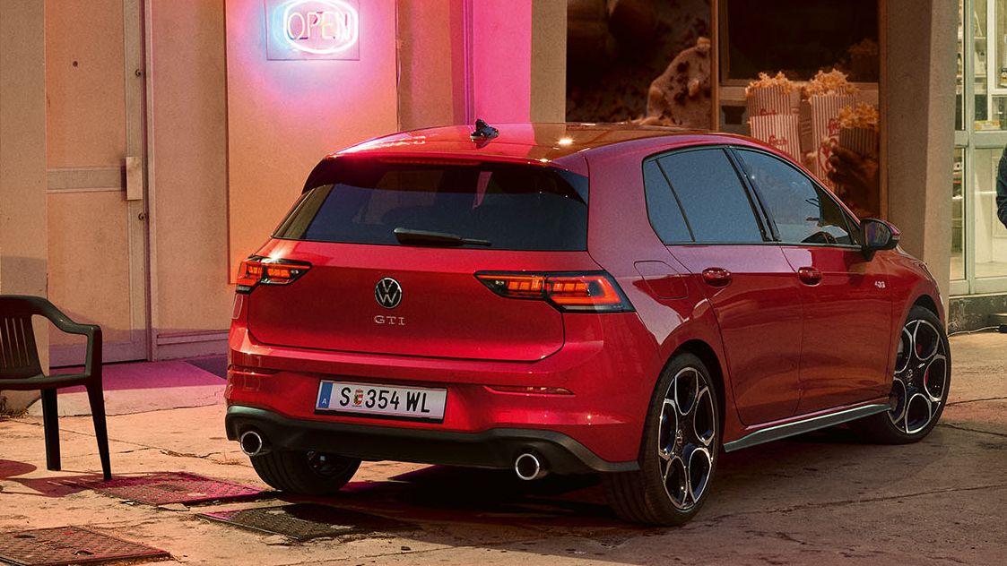 Heckansicht eines roten VW Golf GTI in abendlicher Stimmung, zwei Personen gehen neben ihm her