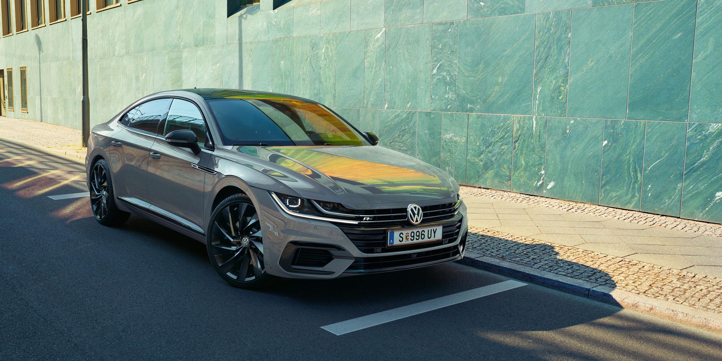 Сив Volkswagen Arteon, паркиран на улица до модерна сграда със зелени фасадни панели