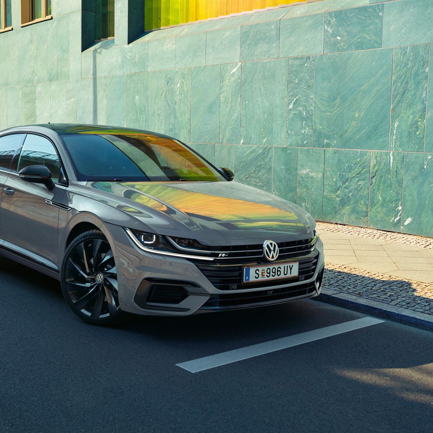 Сив Volkswagen Arteon, паркиран на улица до модерна сграда със зелени фасадни панели