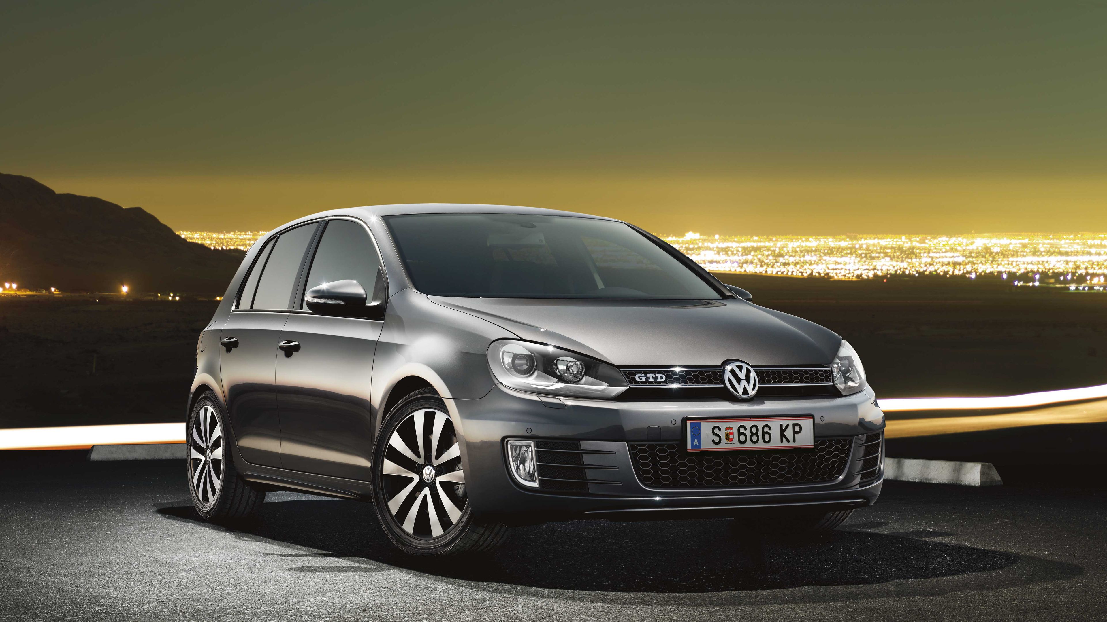 Сив Volkswagen Golf GTD, паркиран на открито с блестящ градски хоризонт на заден план през нощта