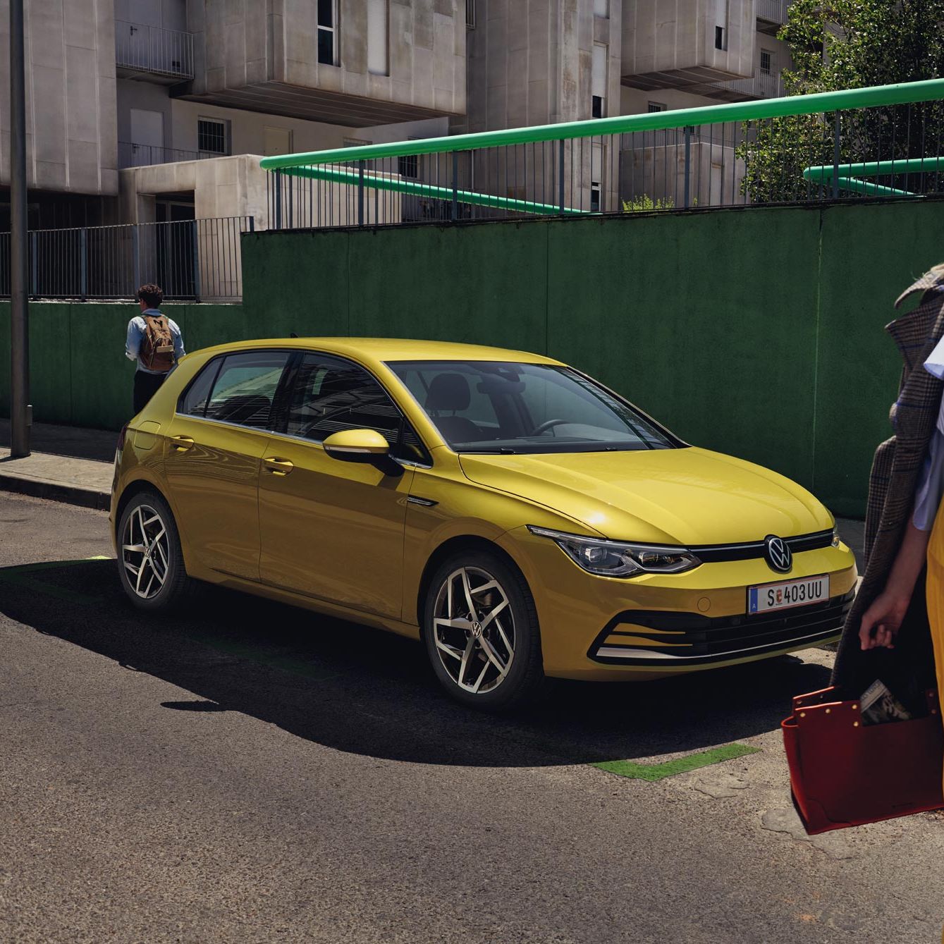 Жълт Volkswagen Golf паркиран на градска улица с модерно облечена жена на преден план