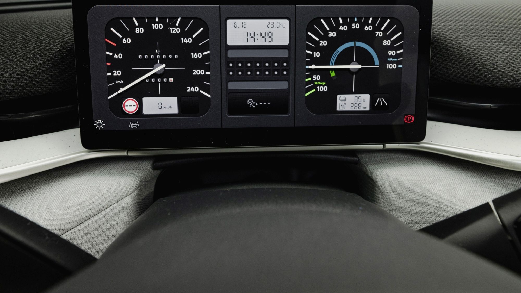 Изображението показва приборното табло на автомобил с два аналогови скоростомера и цифров дисплей, показващ час. Таблото е модерно и има различни индикатори за състоянието на автомобила. Небето се вижда през предното стъкло.