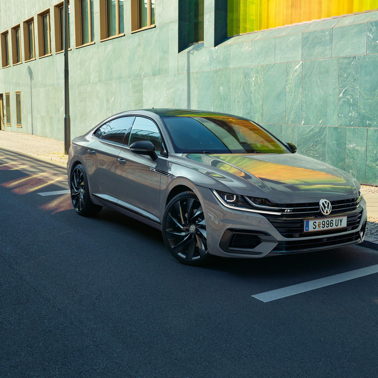 Сив Volkswagen Arteon, паркиран на улица до модерна сграда със зелени фасадни панели