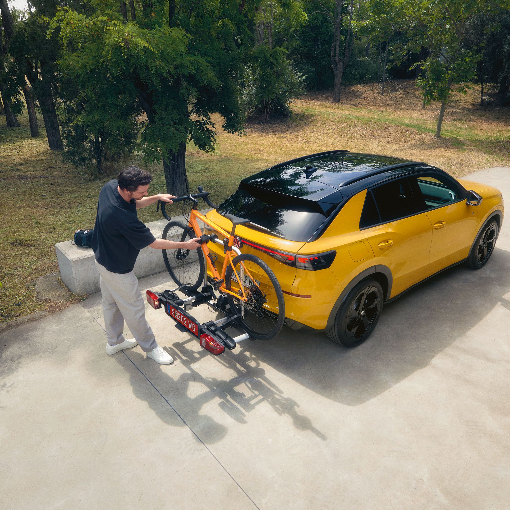 Мъж закрепя велосипед на багажник за колела върху жълт Volkswagen T-Roc.