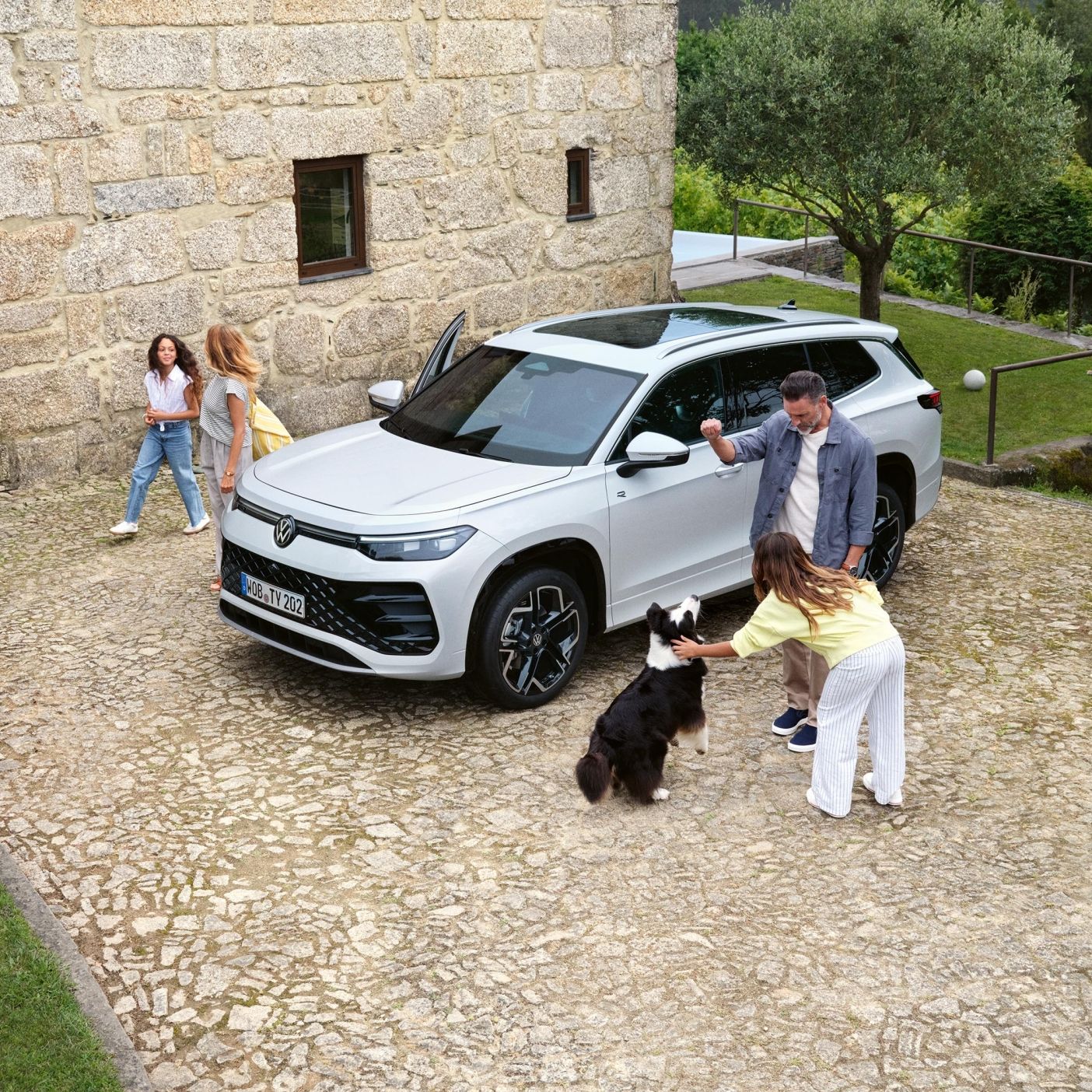 Семейство с куче пред къща до паркиран бял Volkswagen Tayron