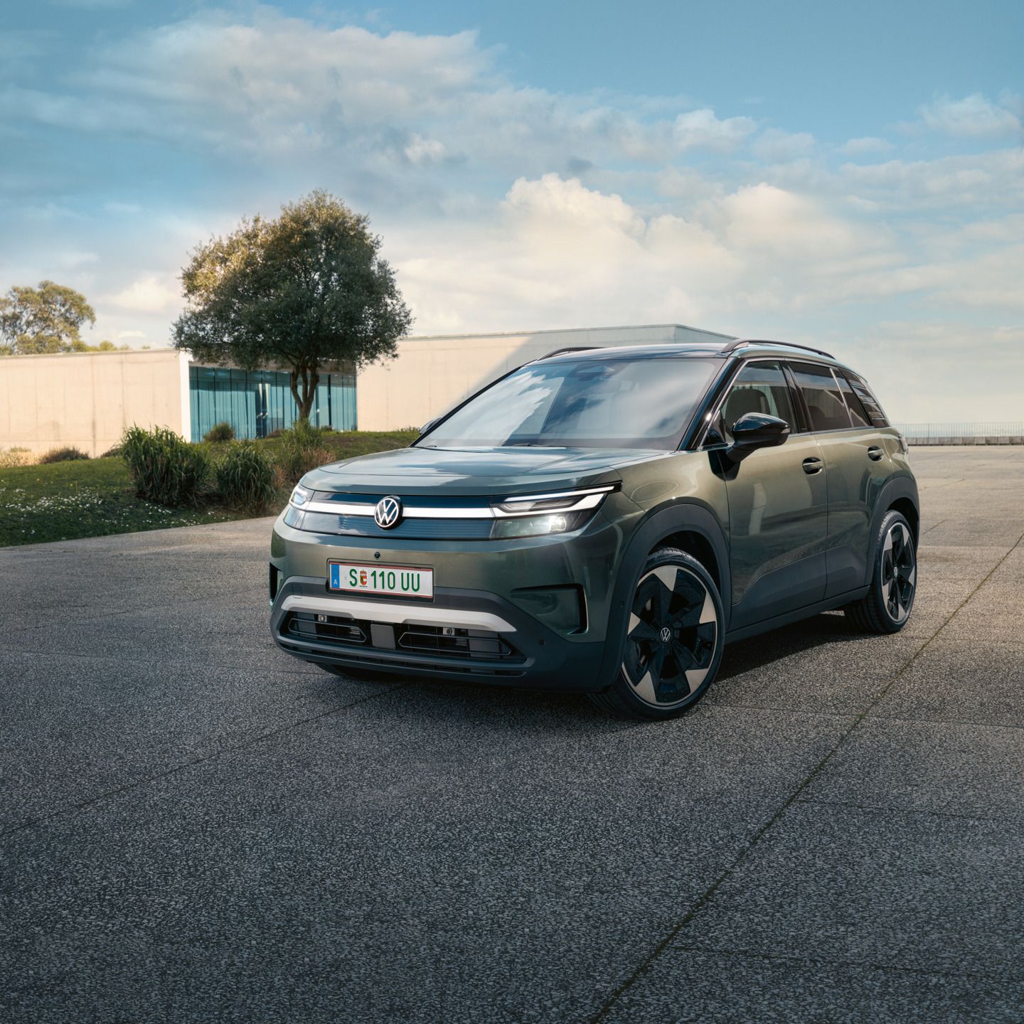 Зелен VW ID. Cross стои пред модерна стъклена сграда върху бетонна повърхност.