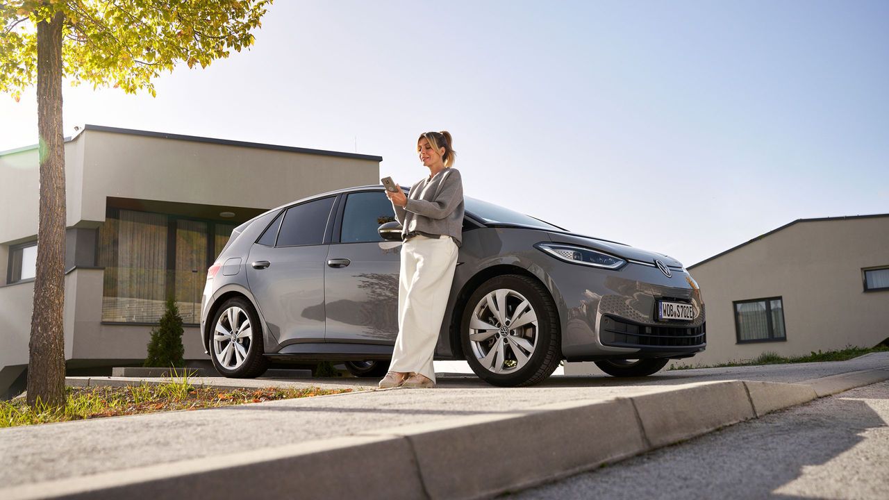 Жена се е облегнала на своя ID.3 автомобил и гледа телефона си