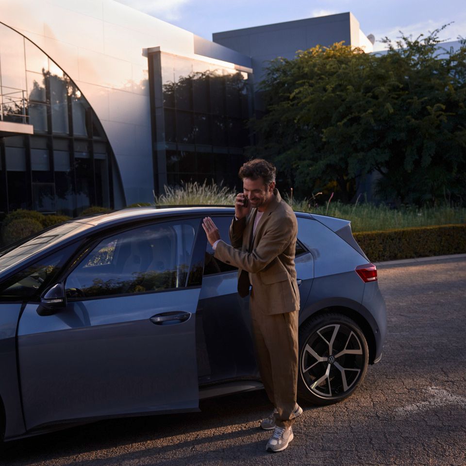 Мъж стои пред син VW ID.3 Neo и прави телефонно обаждане на смартфона си