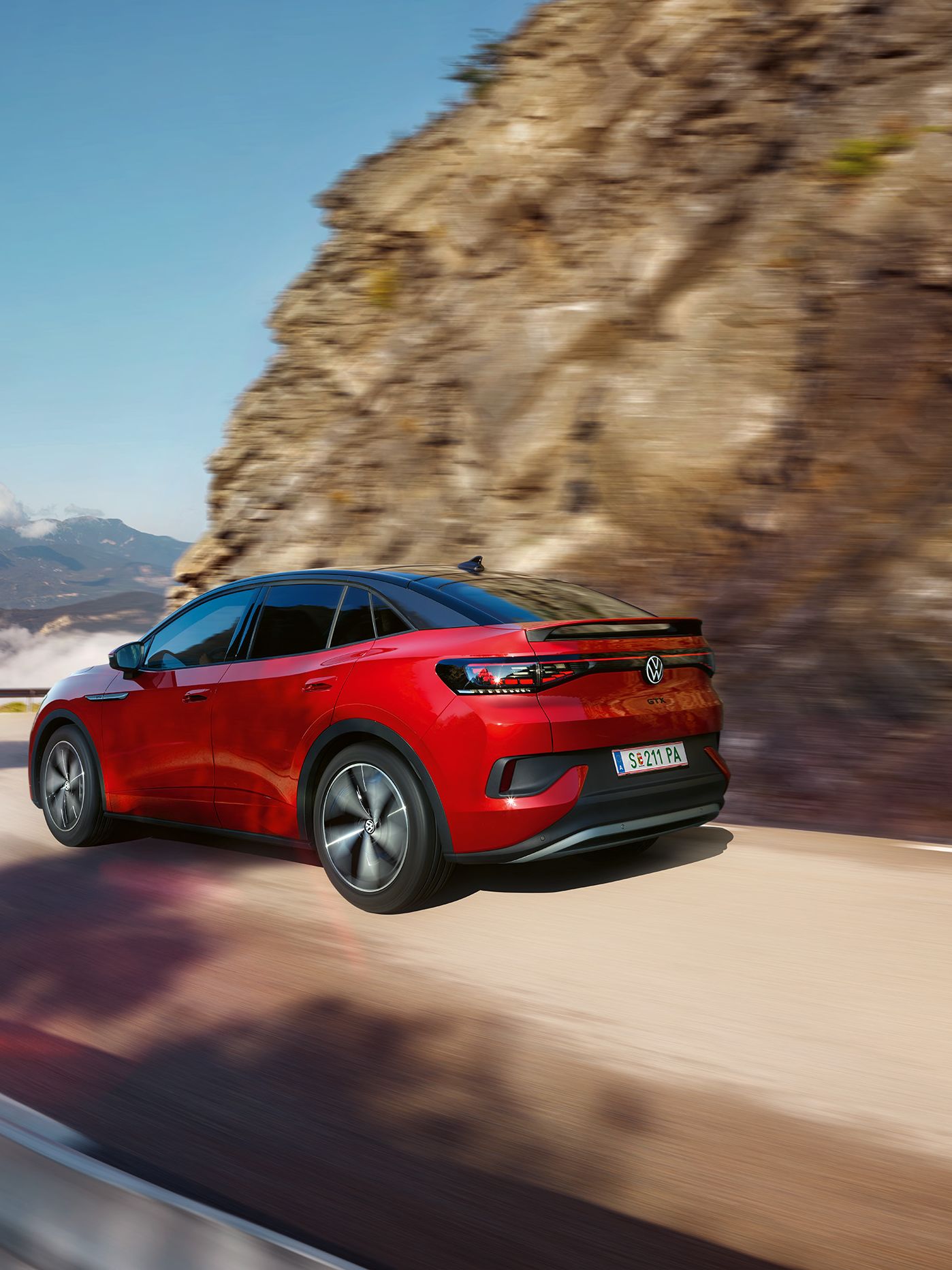 Червен VW ID.5 GTX се движи динамично по планински път. Поглед към предницата, колелата и задната част на автомобила.