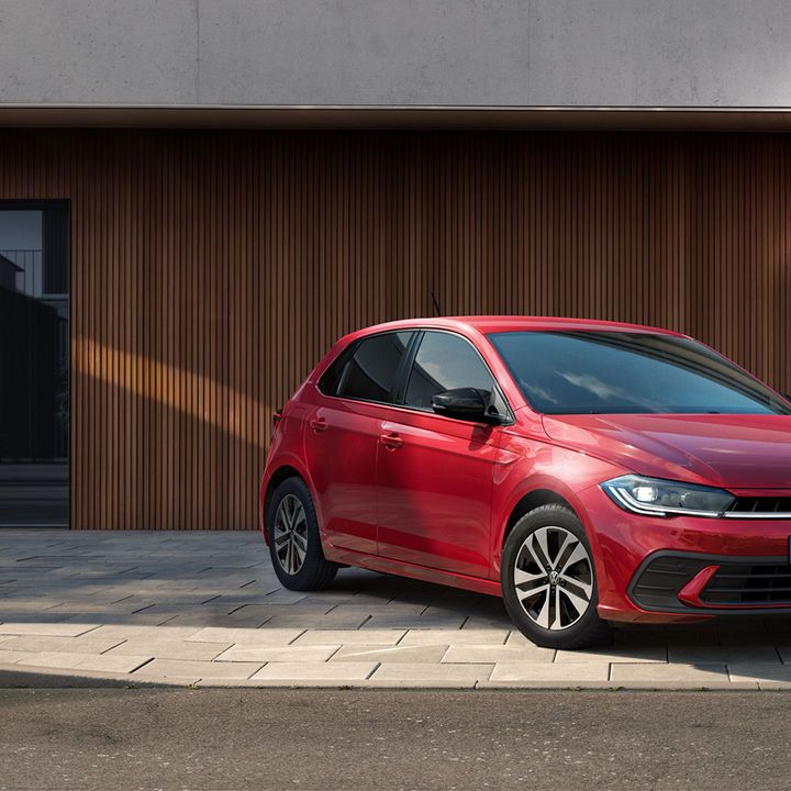 Червен Volkswagen Polo паркиран пред модерен градски дом с дървена фасада